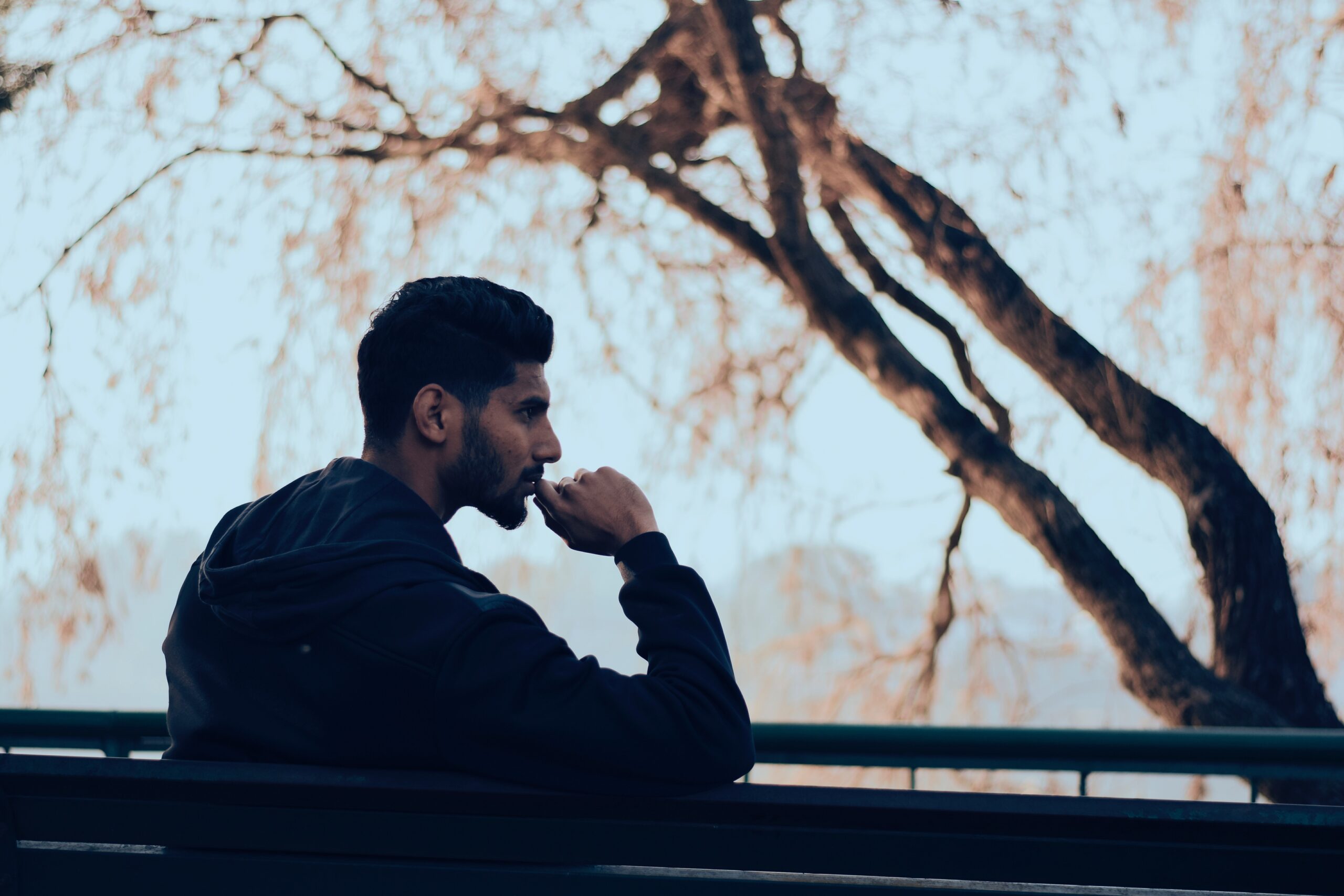 man in black hoodie sitting on bench near green trees 819635 scaled