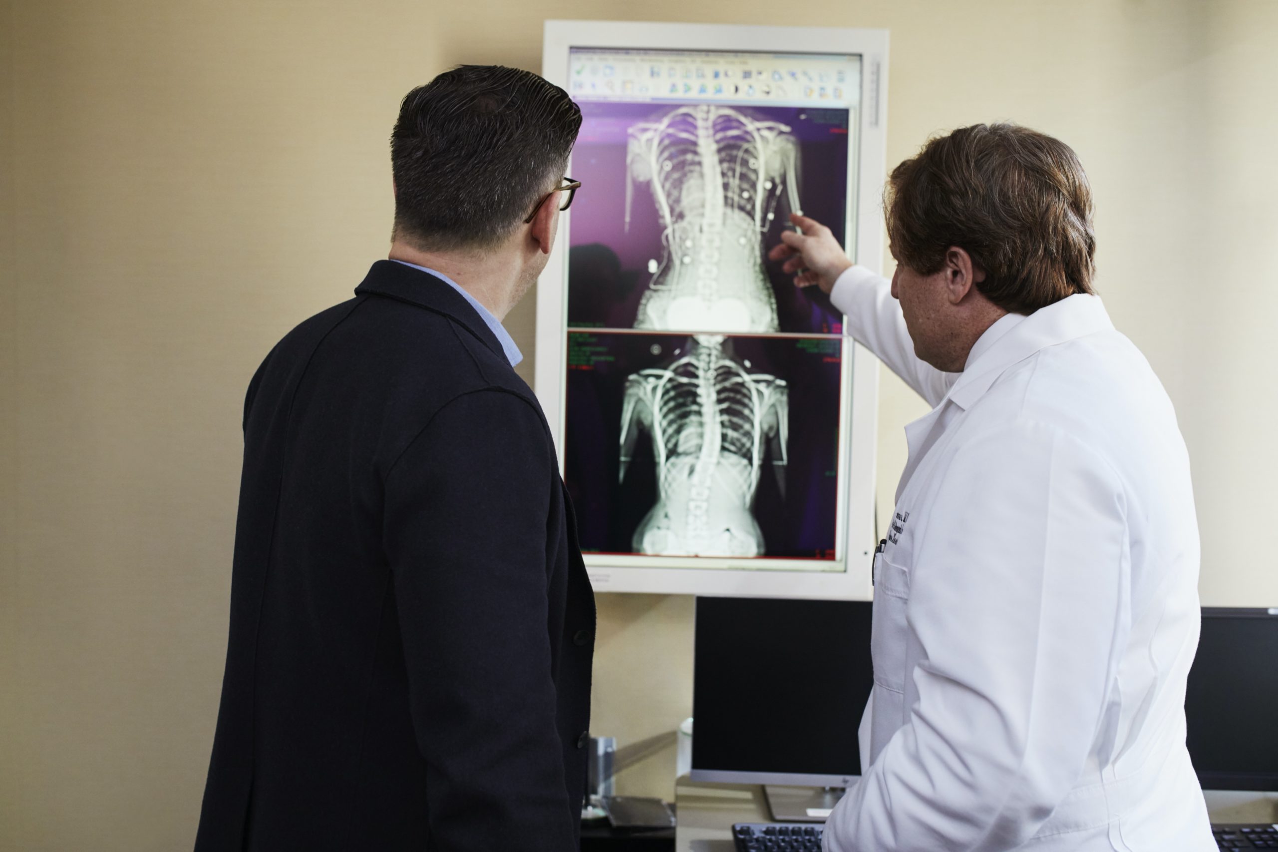 doctor pointing x ray result beside man wearing black suit 2182972 1 scaled 1