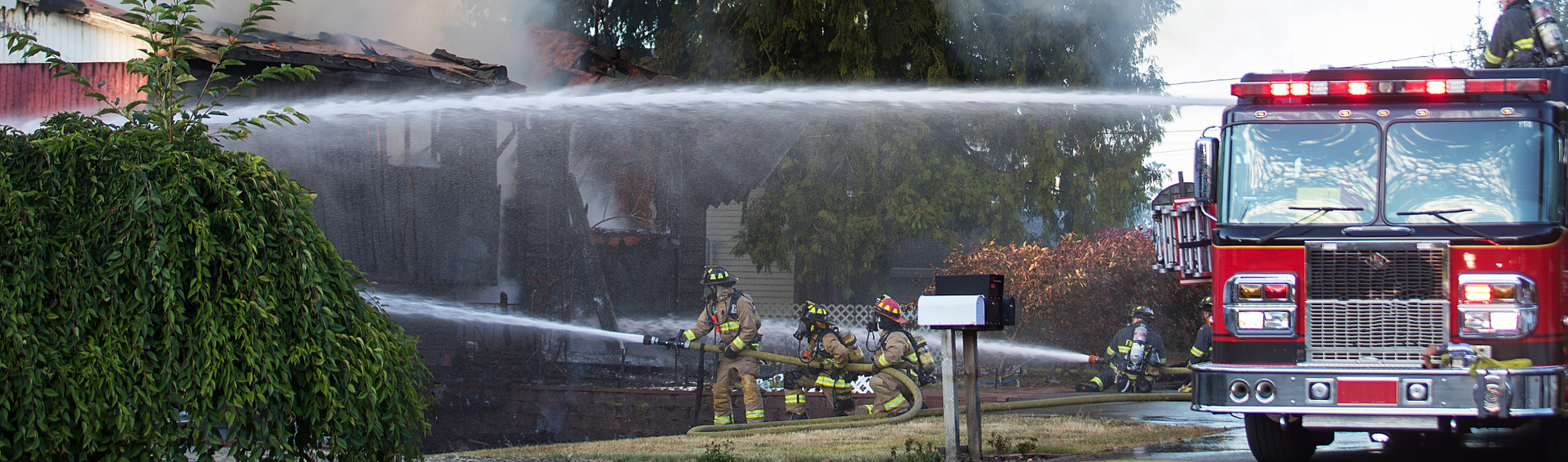 A residential home burns in a house fire as firefighters spay water from a hose in an effort to put it out