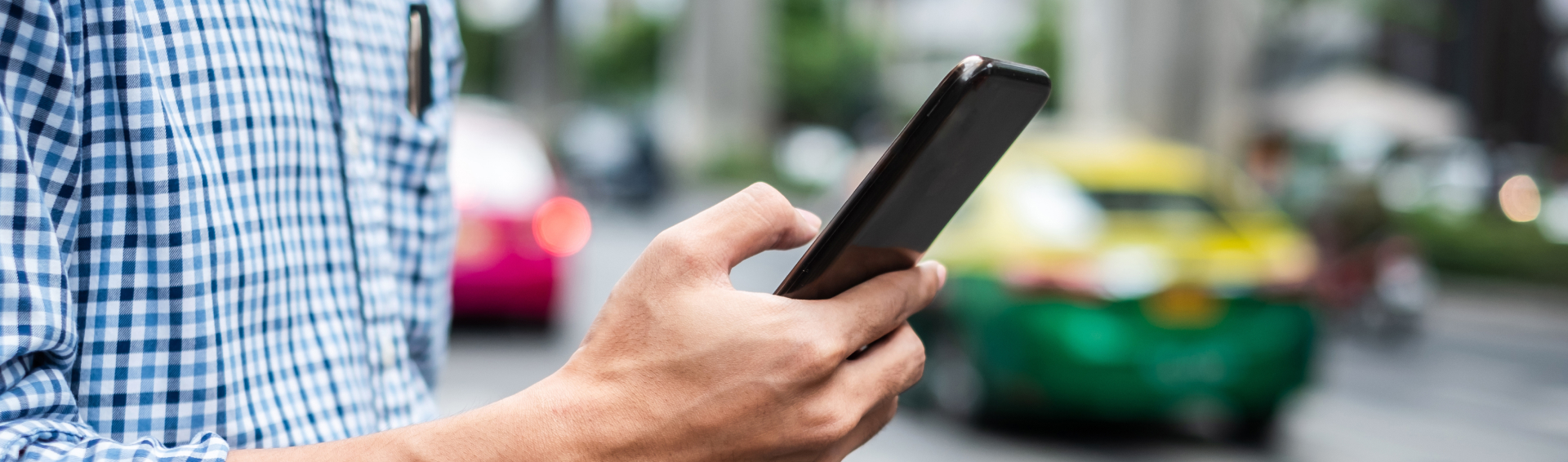 Young man tourist or casual businessman ordering taxi via cab application on smartphone in city street